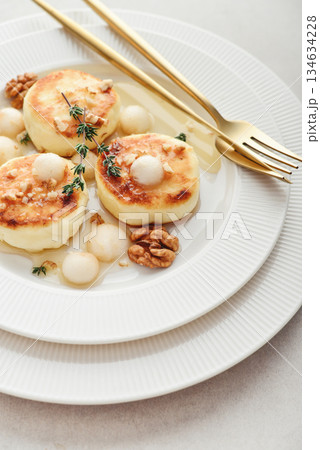 cottage cheese pancakes, syrniki, curd fritters served with pear balls, walnut and honey 134634228
