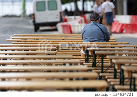 Person sitting alone on wooden bench during outdoor event Person sitting alone on wooden bench during outdoor event 134634721