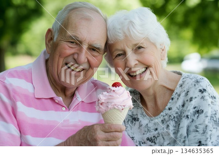 A joyful middle-aged couple enjoys strawberry ice cream together on a sunny day 134635365