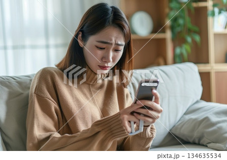 自宅のリビングで体温計を手に持ちスマートフォンでオンライン診療を受ける女性 134635534