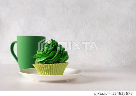 St. Patrick's Day with cup of Irish coffee, chocolate cupcakes decorated green whipped cream and clover on white background for festive holiday. Close up. Copy space. St. Patrick's Day with cup of Irish coffee, chocolate cupcakes decorated green whipped cream and clover on white background for festive holiday. Close up. Copy space. 134635673