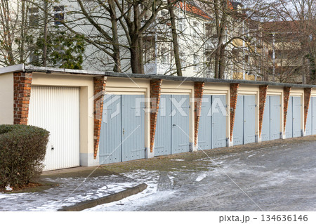 Row residential garages grey doors brick pillars icy driveway German neighborhood during winter season. Urban housing infrastructure scene shows parking storage quiet residential environment Europe Row residential garages grey doors brick pillars icy driveway German neighborhood during winter season. Urban housing infrastructure scene shows parking storage quiet residential environment Europe 134636146
