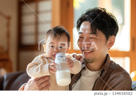 明るいリビングで赤ちゃんを抱っこして哺乳瓶でミルクをあげる優しい父親 134638582