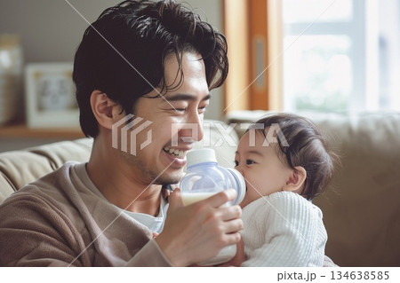 明るいリビングで赤ちゃんを抱っこして哺乳瓶でミルクをあげる優しい父親 134638585