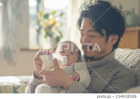 明るいリビングで赤ちゃんを抱っこして哺乳瓶でミルクをあげる優しい父親 134638589