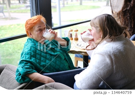 Two Diverse Young Women Enjoying a Meal and Drinks Together at a Cozy Cafe by the Window on a Bright Afternoon Two Diverse Young Women Enjoying a Meal and Drinks Together at a Cozy Cafe by the Window on a Bright Afternoon 134640759