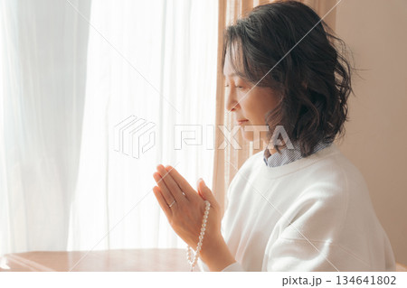 自宅で故人に祈りを捧げるミドル女性 134641802