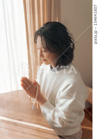 自宅で故人に祈りを捧げるミドル女性 134641807