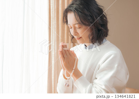 自宅で故人に祈りを捧げるミドル女性 134641821