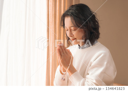 自宅で故人に祈りを捧げるミドル女性 134641823