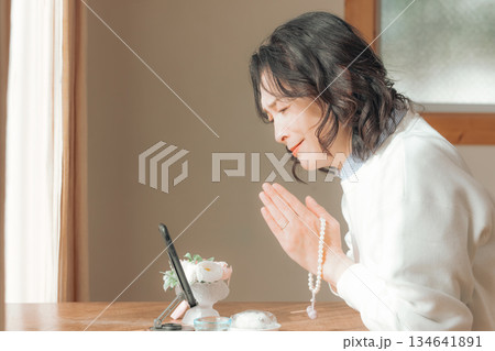 自宅で故人に祈りを捧げるミドル女性 134641891