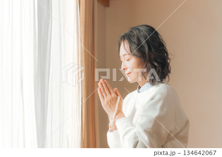 自宅で故人に祈りを捧げるミドル女性 134642067