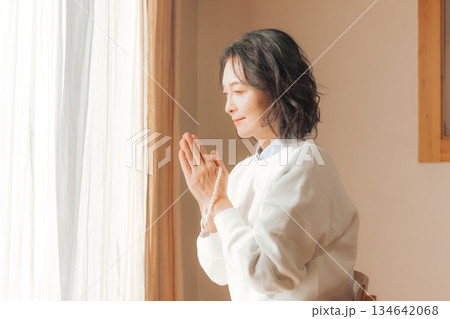 自宅で故人に祈りを捧げるミドル女性 134642068