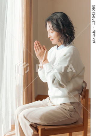 自宅で故人に祈りを捧げるミドル女性 134642069