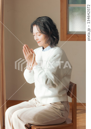 自宅で故人に祈りを捧げるミドル女性 134642072