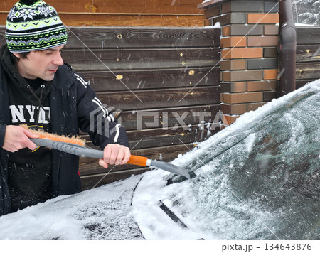 Man cleaning car from snow and ice with brush and scraper on winter morning. Daily routine during cold season. 134643876