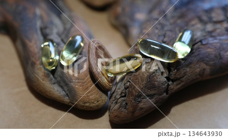 Five golden omega 3 capsules on wooden bark. Health supplement and nutrition concept. Pills for heart health. 134643930