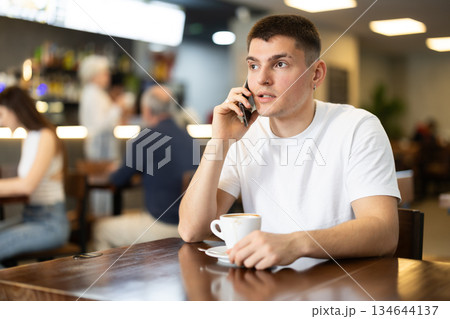 Young man drinking coffee and talking on phone Young man drinking coffee and talking on phone 134644137