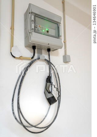 A new electricity meter is mounted on wall, displaying energy usage with a green light. Cables run down, connecting to the meter and hanging nearby. charger for electric car 134646901