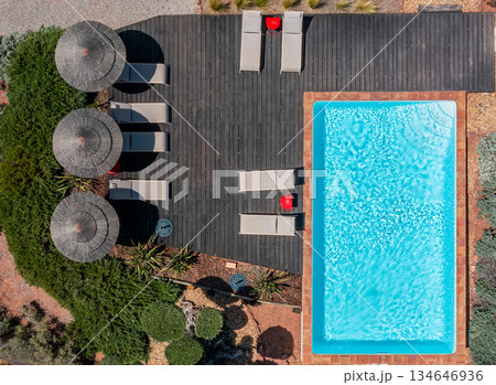 A serene outdoor space includes a clear swimming pool and lounge chairs beneath shaded umbrellas, surrounded by neatly arranged greenery in daylight A serene outdoor space includes a clear swimming pool and lounge chairs beneath shaded umbrellas, surrounded by neatly arranged greenery in daylight 134646936