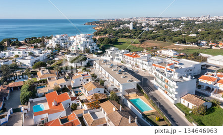Aerial view of Olhos de Agua in Albufeira with white coastal houses, swimming pools and Atlantic Ocean under clear blue sky in Algarve, Portugal. Concept of relaxed seaside living and tourism Aerial view of Olhos de Agua in Albufeira with white coastal houses, swimming pools and Atlantic Ocean under clear blue sky in Algarve, Portugal. Concept of relaxed seaside living and tourism 134646963