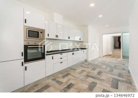A bright and airy kitchen features white cabinets, a black countertop, and modern appliances, creating an inviting space for cooking and gatherings 134646972