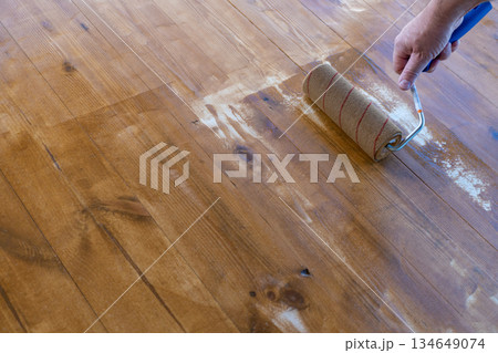 Hand applying varnish on wooden floor with roller for smooth finish 134649074