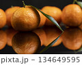 fresh orange small tangerines with green leaves are reflected on a black mirror , a group of ripe sweet tangerines with green leaves with reflection on a black glass 134649595