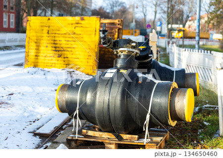 Insulated heating pipeline valves pallets urban site during winter energy maintenance utility. District heating equipment shows steel pipes, safety control technology public utility supply Germany Insulated heating pipeline valves pallets urban site during winter energy maintenance utility. District heating equipment shows steel pipes, safety control technology public utility supply Germany 134650460