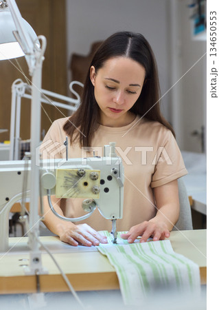 A Focused Seamstress Diligently Working with a Sewing Machine in Her Creative Workspace A Focused Seamstress Diligently Working with a Sewing Machine in Her Creative Workspace 134650553
