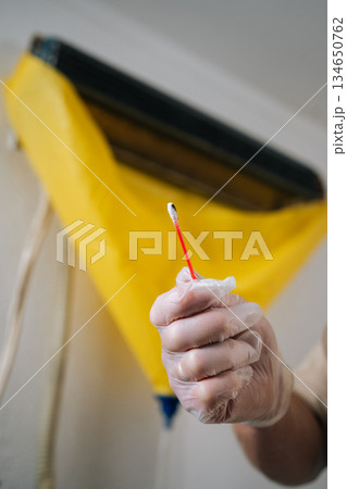 Closeup vertical cropped shot of technician in gloves cleaning mold from dirty air conditioner with cotton swab, promoting proper hygiene and ensuring maintenance for improved indoor air quality. 134650762