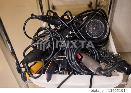 Chaotic styling station, Messy salon tools and cables, Disorganized hair dryer and equipment setup, Cluttered collection of salon devices and tangled wiring mess 134651914