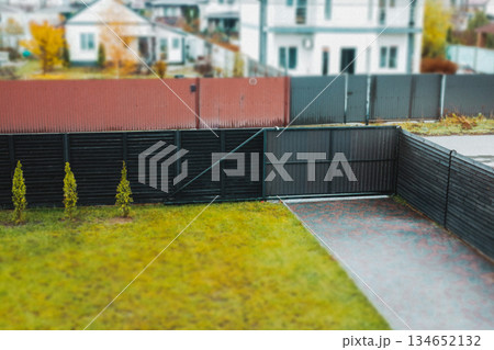 Modern home exterior with a black fence and gate, green lawn in a residential neighborhood. Well-maintained yard, real estate or home design projects. 134652132