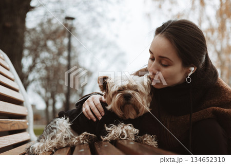 Woman spending time with her Yorkshire Terrier small dog, doggy outdoors in autumn park. Emotional bond of human and pet, and fall season mood. 134652310