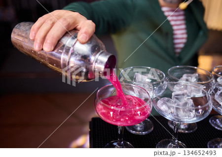 Mood setting with lively drink preparation at upscale bar, Elegant scene of bartender pouring colorful cocktail amidst festive warm lighting and guests in background Mood setting with lively drink preparation at upscale bar, Elegant scene of bartender pouring colorful cocktail amidst festive warm lighting and guests in background 134652493