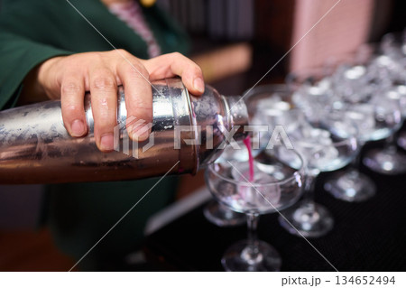 Mood setting with lively drink preparation at upscale bar, Elegant scene of bartender pouring colorful cocktail amidst festive warm lighting and guests in background Mood setting with lively drink preparation at upscale bar, Elegant scene of bartender pouring colorful cocktail amidst festive warm lighting and guests in background 134652494