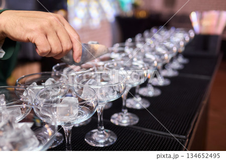 Mood setting with lively drink preparation at upscale bar, Elegant scene of bartender pouring colorful cocktail amidst festive warm lighting and guests in background 134652495