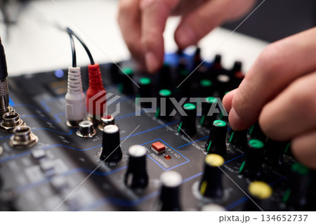 Closeup of hands adjusting mixer with glowing LED indicators and cables, Detailed image of operator controlling mixer dials and monitoring sound through sensors and LEDs 134652737