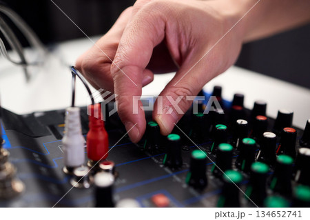 Closeup of hands adjusting mixer with glowing LED indicators and cables, Detailed image of operator controlling mixer dials and monitoring sound through sensors and LEDs 134652741