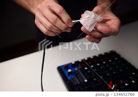 Personnel meticulously maintain audio equipment hygiene, Detailed shot of technician carefully cleaning audio cable with soft cloth in professional studio environment 134652760