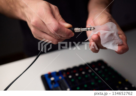 Personnel meticulously maintain audio equipment hygiene, Detailed shot of technician carefully cleaning audio cable with soft cloth in professional studio environment 134652762