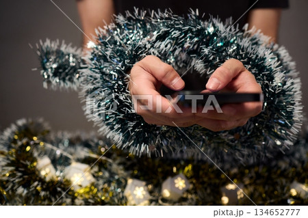 Digital holiday planning, Person reviewing online presents on tabletop, Warm indoor scene of individual managing digital gift list amidst festive lights and ornaments 134652777