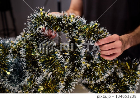 Closeup of hands preparing decorations, People arranging sparkling tinsel for celebration, Individuals meticulously position shimmering tinsel for seasonal festivity setup 134653239