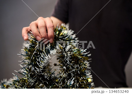 Closeup of hands preparing decorations, People arranging sparkling tinsel for celebration, Individuals meticulously position shimmering tinsel for seasonal festivity setup 134653240