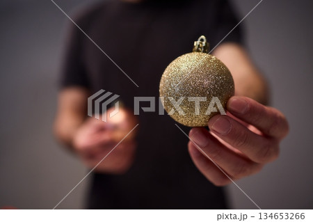 Hands arranging Christmas New Year baubles on white table with tinsel and warm bokeh lights, metallic red gold pink palette, careful styling by home decorator, festive craft mood 134653266