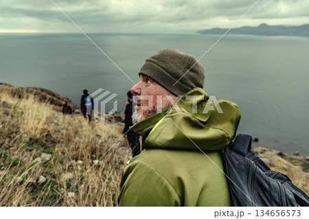Hikers exploring a rugged coastline under a cloudy sky near the ocean in a remote location Hikers exploring a rugged coastline under a cloudy sky near the ocean in a remote location 134656573