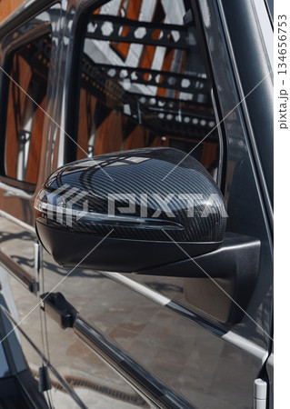Close-up of a luxury car mirror showcasing sleek carbon fiber design in bright sunlight 134656753