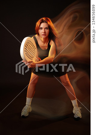 Woman playing sport in dynamic pose with a racket and focused expression indoors 134656899