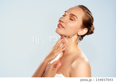 Woman applying cream to her skin while smiling and enjoying the moment in a studio setting Woman applying cream to her skin while smiling and enjoying the moment in a studio setting 134657043
