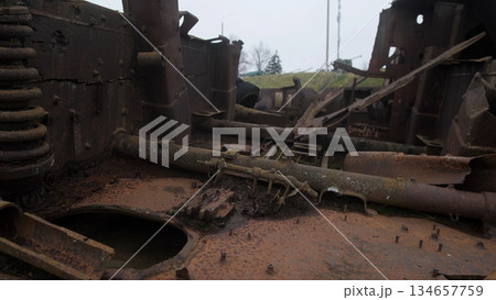 abandoned rusted military vehicle interior, salvage crew survey site amid corroded hull and torn seats, scattered debris and twisted metal, moss and vegetation reclaiming surfaces, dust-filled shafts 134657759